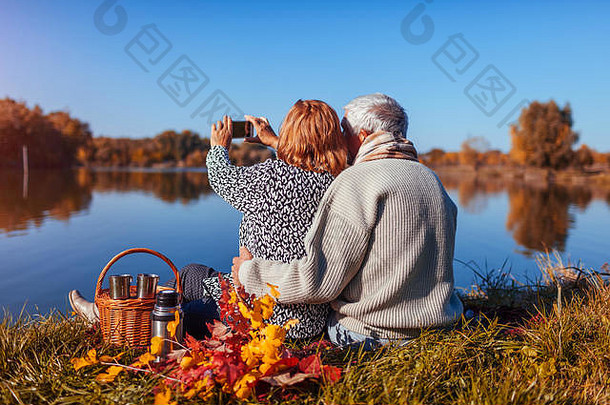 高级夫妇采取自拍电话野餐秋天湖快乐男人。女人享受自然拥抱