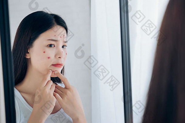 年轻的亚洲女人挤压痤疮问题脸镜子护肤品