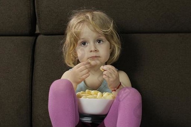 美丽的金发女郎女孩坐着沙发首页吃玉米泡芙可爱的孩子味道puffcorns内部<strong>儿童餐</strong>