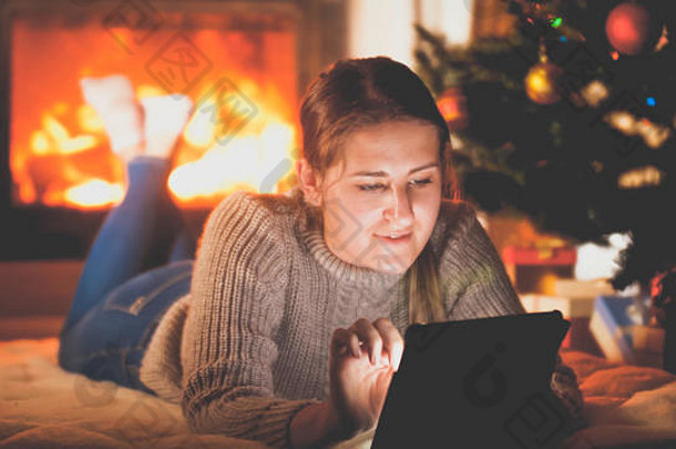 健美的肖像微笑女人平板电脑说谎地板上firepalce圣诞节树