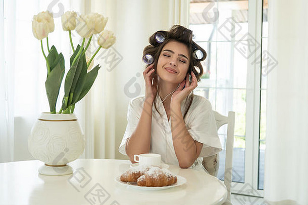美丽的年轻的微笑浅黑肤色的女人头发卷发器听音乐早餐明亮的厨房