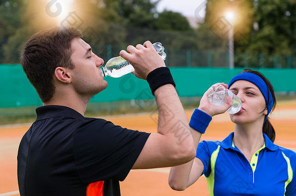 年轻的夫妇网球球员穿运动服装喝水匹配户外粘土法院在户外