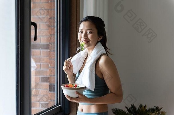 年轻的亚洲女人吃健康的绿色蔬菜窗口
