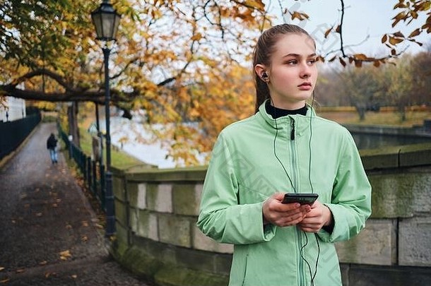 有吸引力的运动女孩耳机手机走运行秋天公园