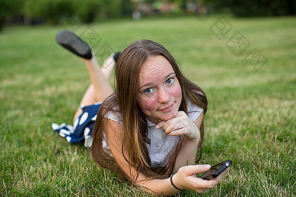 可爱的青少年女孩智能手机手说谎绿色草相机