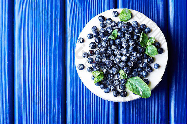 甜蜜的奶油蓝莓芝士蛋糕新鲜的蓝莓薄荷叶子蓝色的木背景复制空间前视图