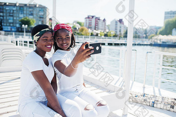 时尚的时尚的非洲美国女孩穿白色衣服湖码头海滩使自拍细胞电话街时尚年轻的