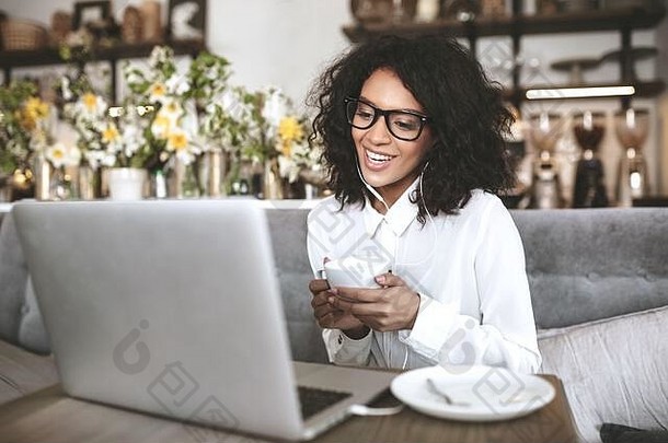 年轻的非洲美国女孩眼镜坐着餐厅移动PC杯咖啡手微笑女孩黑暗卷曲的头发