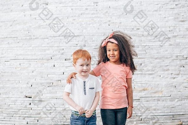 红色头发的人男孩非洲女孩站前面白色砖墙女孩把手肩膀男孩概念童年朋友