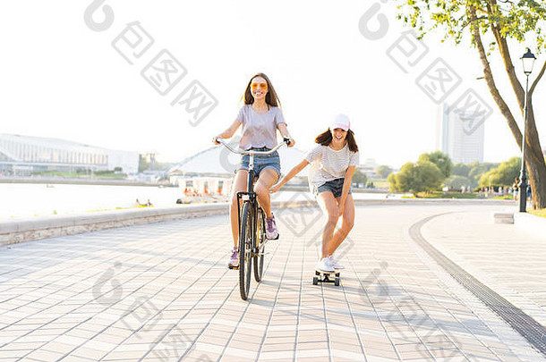 可爱的笑年轻的女人牛仔裤短裤自行车拉女孩持有滑板
