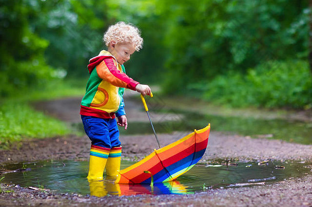 男孩玩多雨的夏天公园孩子色彩斑斓的彩虹伞防水外套靴子跳水坑