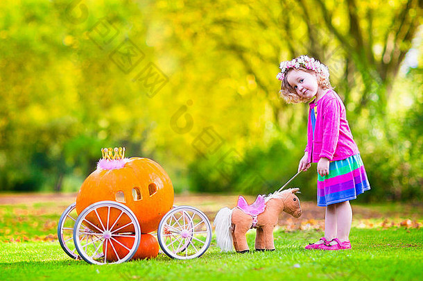 可爱的卷曲的女孩玩灰姑娘仙女演讲持有魔法魔杖南瓜马车有趣的秋天公园