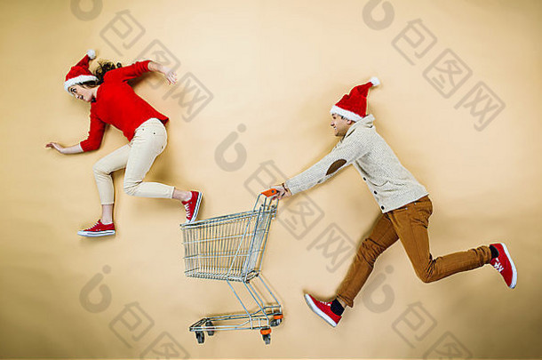 年轻的夫妇圣诞节帽子有趣的运行购物电车米色背景