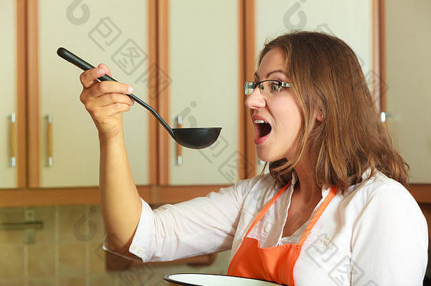 家庭主妇品尝汤餐晚餐中间岁的女人持有勺子包能管家穿橙色围裙准备食物