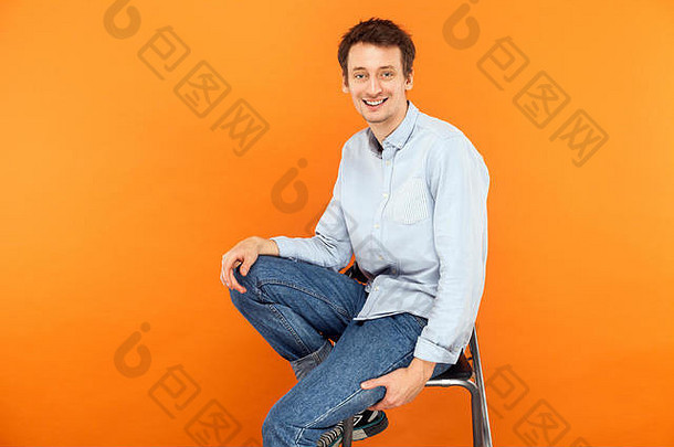 幸福男人。<strong>坐椅子</strong>相机露出牙齿的微笑工作室拍摄橙色背景