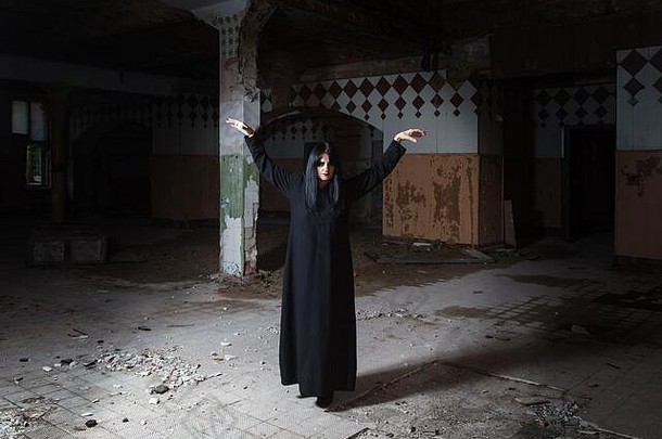 哥特浅黑肤色的女人女人提高手站大空大厅黑暗悲观的被遗弃的房子