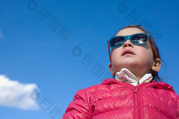 肖像可爱的年蹒跚学步的女孩时尚孩子们太阳镜外套蓝色的天空云背景
