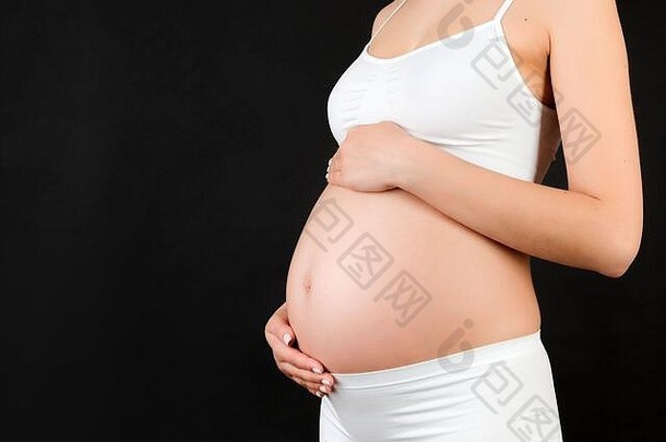 关闭怀孕了女人触碰腹部黑色的背景未来妈妈。穿白色内衣<strong>期待</strong>婴儿复制空间