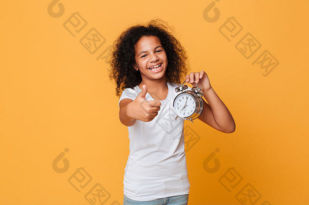 肖像快乐非洲女孩持有报警时钟显示拇指手势孤立的橙色背景
