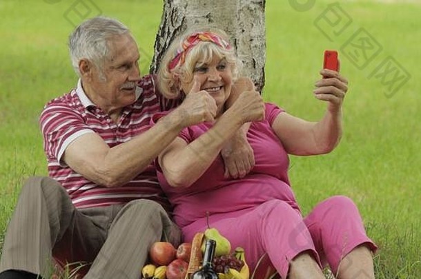 家庭周末野餐人快乐高级高加索人夫妇智能手机使自拍远程在线视频闲谈，聊天调用电话上了年纪的男人。女人丈夫妻子公园爷爷奶奶