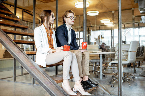 年轻的多少男人。女人谈话坐着<strong>楼梯</strong>咖啡打破现代办公室