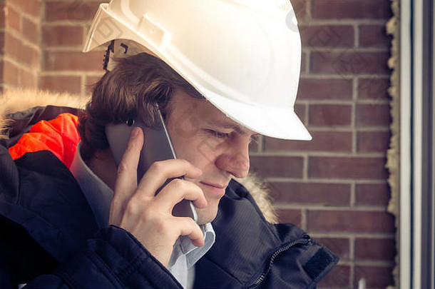 建设检查员白色头盔会说话的移动电话棕色（的）砖墙背景软焦点健美的关闭