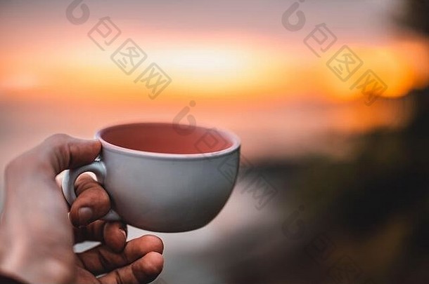 人持有咖啡杯手令人惊异的日落观点拍摄