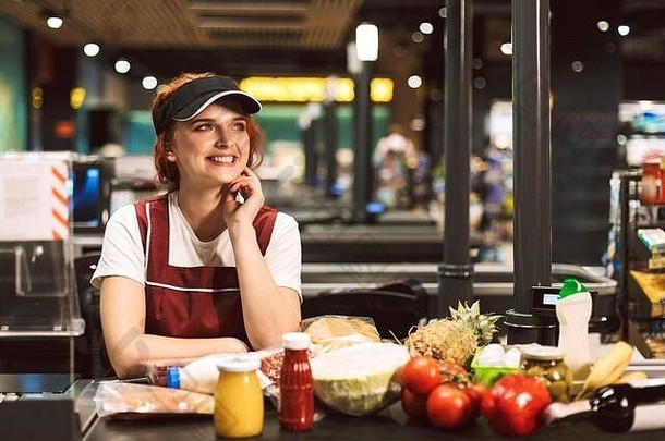 年轻的快乐的女收银员统一的快乐产品现金行工作现代超市