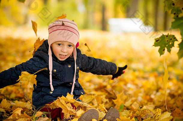 坐着年轻的女孩开玩笑地扔头彩色的枫木叶子可爱的孩子有趣的秋天公园爱秋天色彩斑斓的秋天季节概念秋天快乐童年