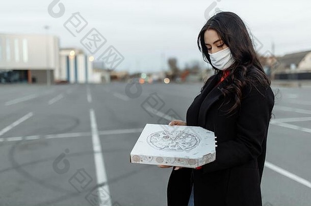 年轻的女人医疗面具持有纸板披萨的食物疫情概念外卖食物检疫