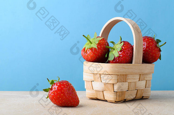 新鲜的红色的草莓堆高填充<strong>小编</strong>织篮子木表面光蓝色的背景