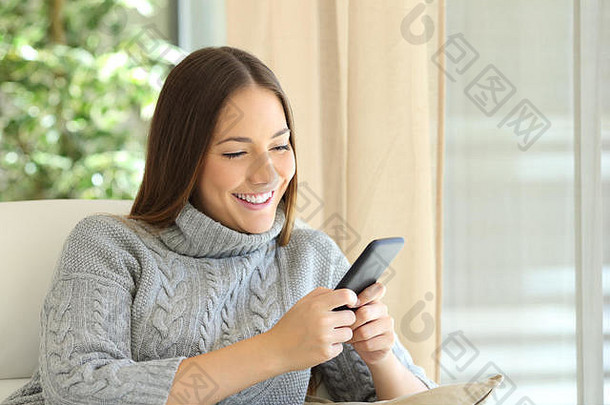 快乐女人穿泽西岛发短信聪明的电话坐着沙发上首页冬天