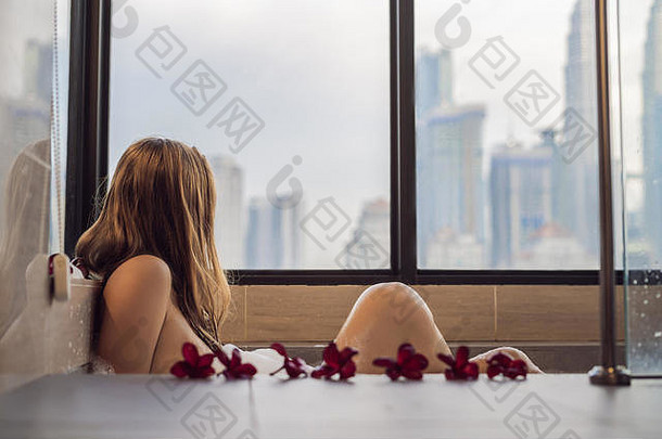 年轻的女人坐在浴泡沫鸡蛋花花背景全景窗口俯瞰摩天大楼大晚上