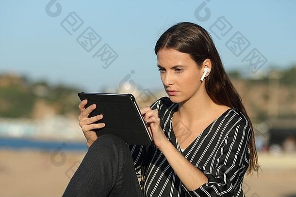 女人电子学习平板电脑无线耳机坐着海岸小镇海滩