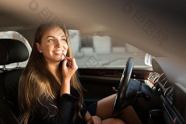 年轻的美丽的微笑女人应用口红坐着车豪华