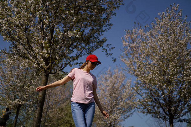 成功的业务女人享受休闲免费的时间公园开花樱花樱桃树穿牛仔裤粉红色的t恤时尚红色的帽
