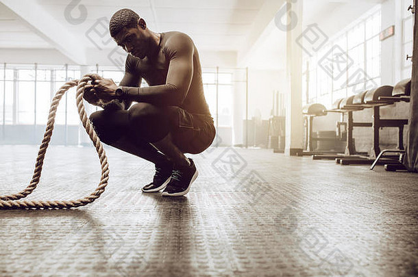 男人。坐着脚趾持有一对战斗绳子锻炼参考的家伙健身房工作健身绳子