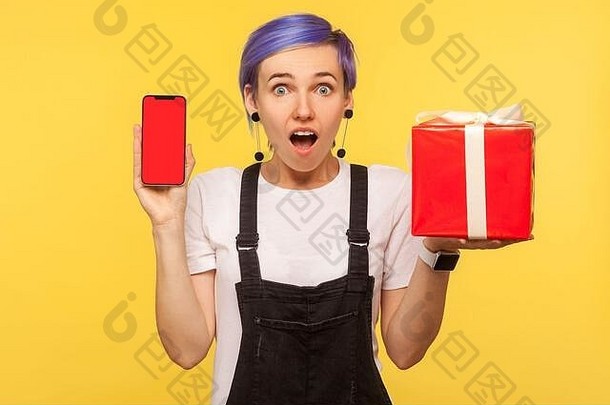 肖像惊讶震惊了赶时髦的人女孩紫罗兰色的短头发工作服持有礼物盒子细胞电话红色的屏幕模拟广告我