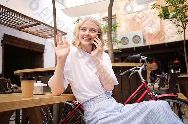 美丽的微笑浪漫的金发碧眼的女孩幸福的会说话的手机问候院子里城市咖啡馆