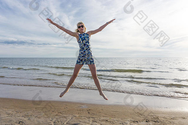 快乐年轻的女人短衣服跳海滩夏天蓝色的天空