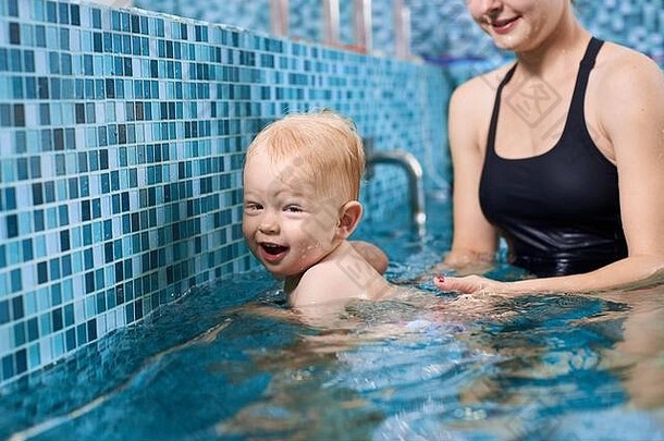 快乐的金发女郎男孩游泳持有银管池妈妈。支持概念休闲体育运动婴儿
