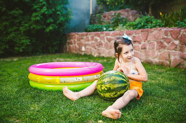 主题适当的健康的吃孩子们婴儿女孩年高加索人坐着绿色草拥抱大绿色轮浆果西瓜孩子们的充气池院子里房子