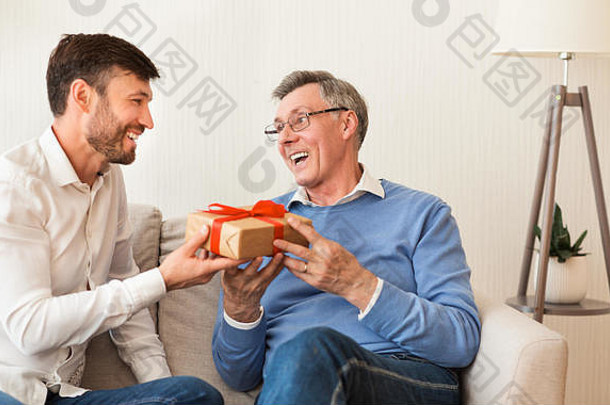 成熟的儿子祝贺上了年纪的父亲给礼物坐着沙发