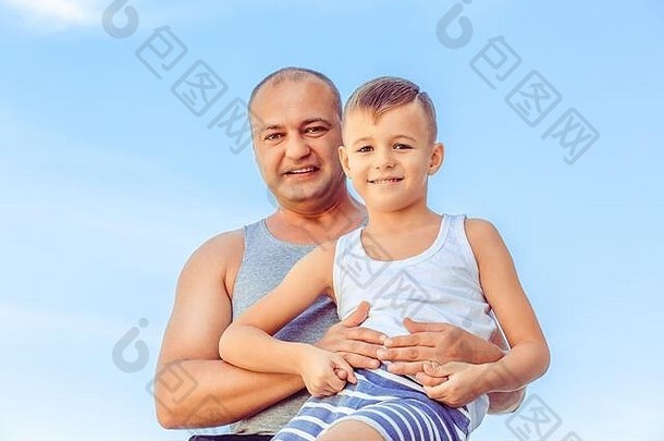 父亲儿子坐着栅栏蓝色的天空背景肖像快乐父亲摆姿势儿子可爱的男孩爸爸玩户外