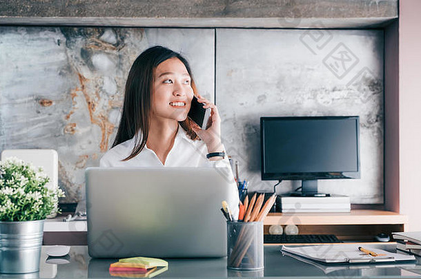 亚洲女商人会说话的移动电话前面移动PC电脑窗口办公室办公室生活方式概念