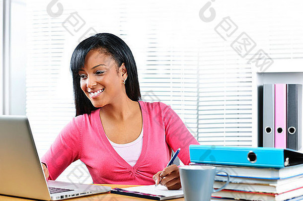 微笑年轻的黑色的女学生电脑教科书桌子上