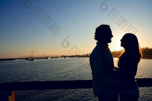轮廓浪漫的夫妇日落前面港海洋