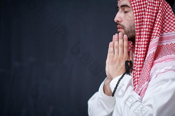 年轻的阿拉伯男人。传统的衣服使传统的祈祷神手祈祷手势前面黑色的黑板代表