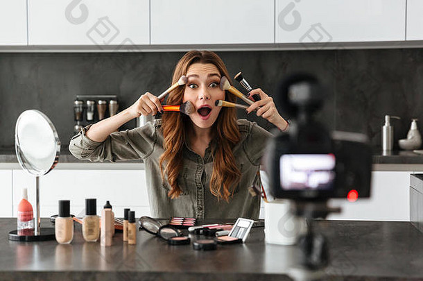 快乐年轻的女孩记录视频博客集化妆品产品坐着厨房表格首页应用化妆