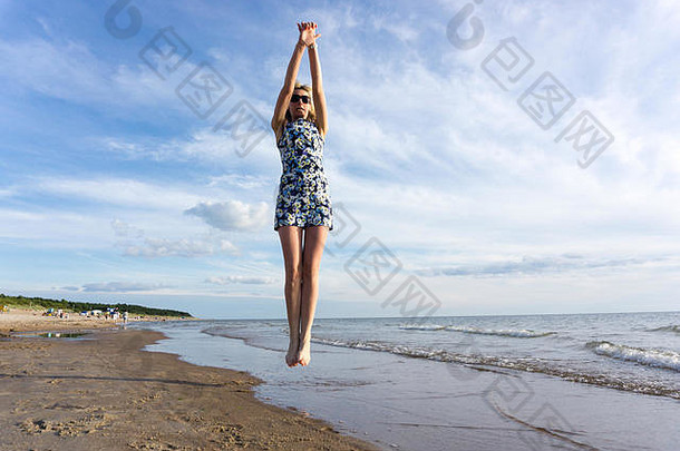 快乐年轻的女人短衣服跳海滩夏天蓝色的天空